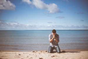 man on his knees praying on the beach - addiction tests faith