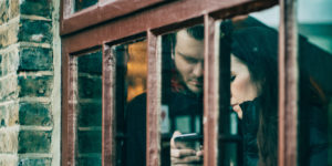 couple looking at same phone, seen through building window - codependency in addiction